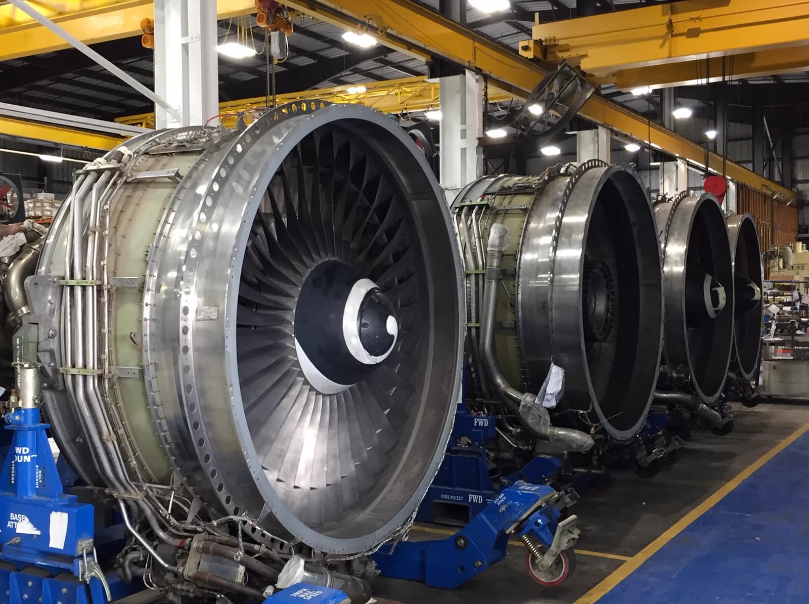A row of turbofan engines on maintenance stands in a modern, softly lit MRO facility