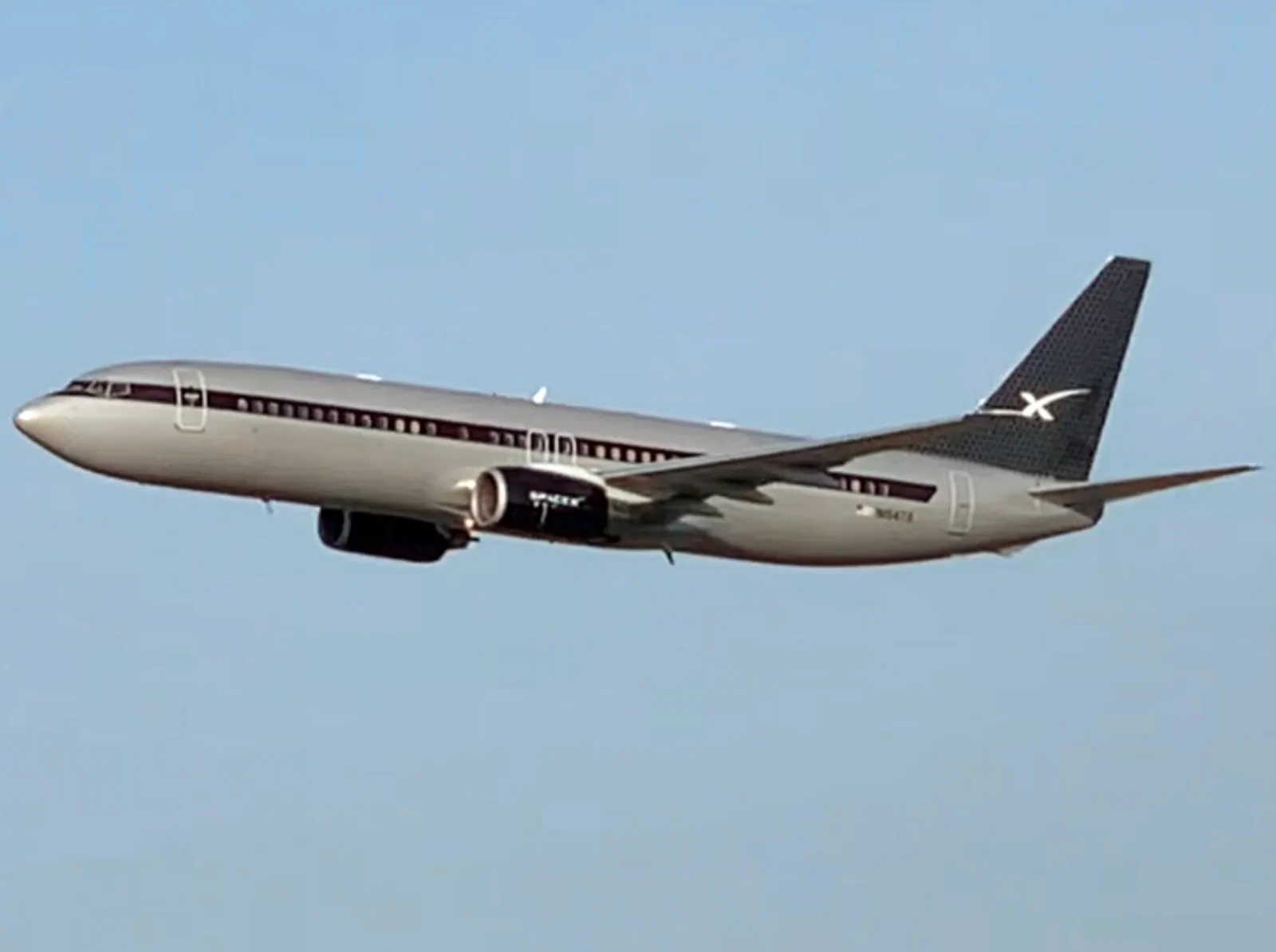 A silver executive Boeing 737 climbing out after takeoff
